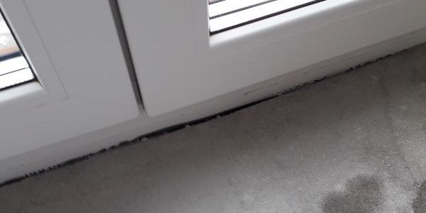 Zbliżenie na dół drzwi balkonowych w miejscu, gdzie spotyka się z posadzką. Widoczny brak uzupełnienia dylatacji między stolarką okienną a podłogą, co udało się odkryć dzięki odbiorowi technicznemu w Olsztynie.