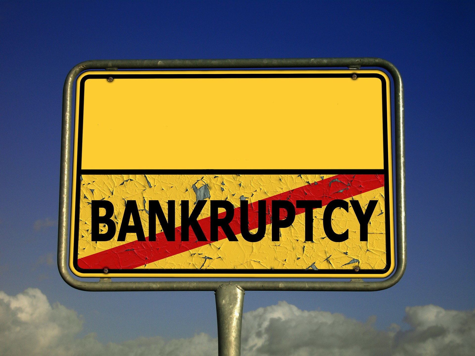 Zniszony, żółty znak drogowy z przekreślonym słowem bankruptcy, który odnosi się do perspektywy upadłości deweloperów.